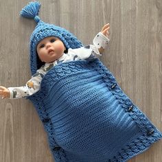 a doll is laying on the floor wearing a blue knitted sleeping bag and hat