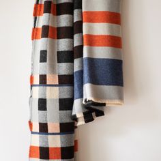 the blanket is hanging up on the wall next to the coat hanger, which also has an orange and blue checkered pattern