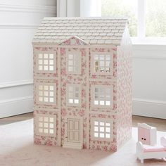 a doll house is sitting on the floor next to a pink chair and window sill