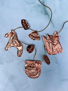 four copper pendants with horse heads and wings on a blue marble background, hanging from a gold cord