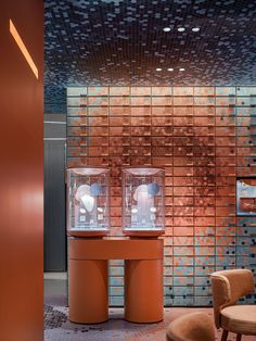 two orange pedestals with clocks on them in front of a brick wall and chairs