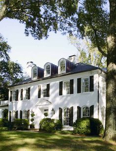 a large white house with black shutters on the front and side windows, surrounded by trees