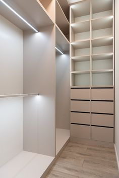 an empty walk in closet with white shelving and lights on the shelves above it