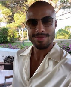 a man wearing sunglasses and a white shirt is posing for a photo in front of some flowers