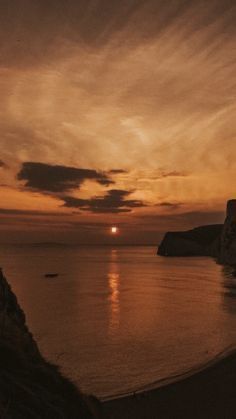 the sun is setting over an ocean with cliffs in the background