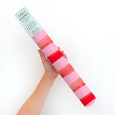 a pink and red striped tube is held up by a person's hand on a white background