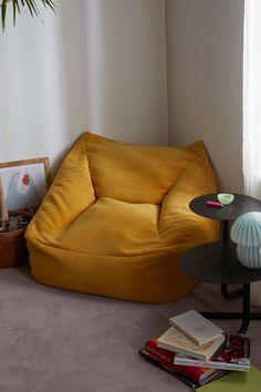 a yellow bean bag chair sitting next to a table with books on it and a potted plant