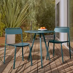 a table and two chairs on a deck with plants in the backround behind them