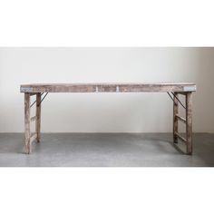 an old wooden table sitting on top of a cement floor next to a white wall