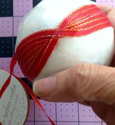 a hand holding a white ball with red thread on it