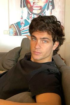 a young man sitting on top of a couch next to a wall with a painting behind him