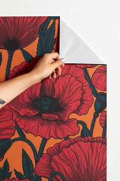 a person's hand is holding an envelope with red flowers on orange and black background