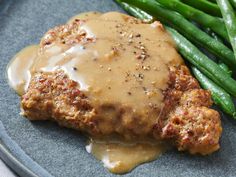 meat with gravy and green beans are on a blue plate, ready to be eaten