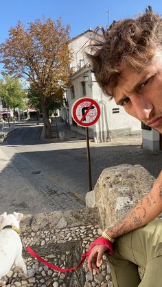 a man sitting next to a white dog on a leash near a no left turn sign