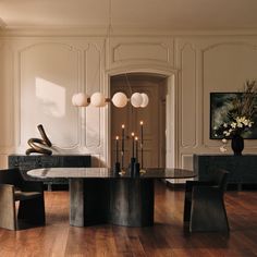 an elegant dining room with wooden floors and white walls, along with black chairs and a round glass table