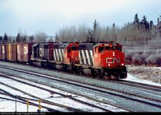 a red train traveling down tracks next to snow covered trees and power lines on a cloudy day