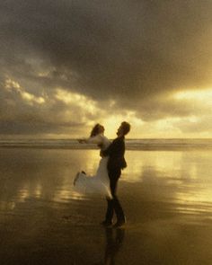 a man and woman walking on the beach at sunset with their arms around each other