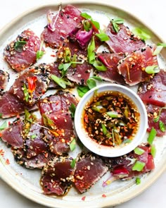 a white plate topped with lots of food on top of a wooden table next to a bowl of sauce