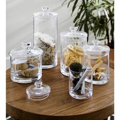 several glass containers with various types of food inside on a wooden table next to a potted plant