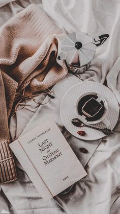 an open book on a bed next to a cup of coffee and some other items