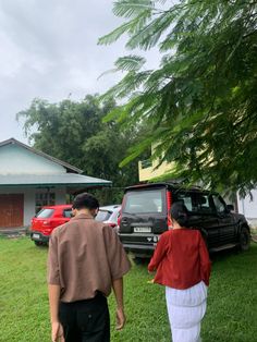 a man and woman walking in front of a house with cars parked on the lawn