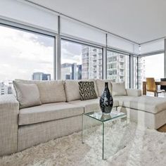 a living room filled with furniture next to tall windows and a wooden floor covered in white fluffy rugs