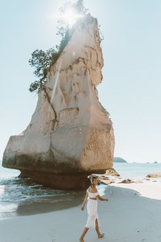 a woman walking on the beach in front of a rock formation