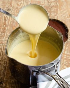 a pot filled with liquid sitting on top of a wooden table next to a spoon