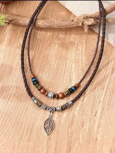 three different necklaces with beads and charms on a wooden table next to a plant