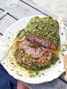 a white plate topped with meat covered in pesto and sauce next to a spoon