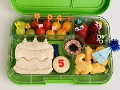 a green lunch box filled with fruit and veggies on top of a white table