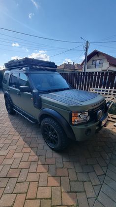 a green land rover is parked in front of a wooden fence and some cars on the street