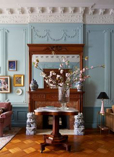 a living room with blue walls and wooden flooring is furnished with antique furniture, flowers in a vase on the coffee table