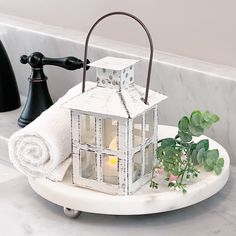 a white candle holder with a house on it sitting on a bathroom counter next to a towel