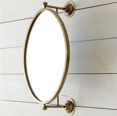 an oval mirror mounted to the side of a white wall with wood planks behind it