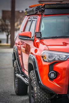 the front end of a bright orange toyota 4x4 with its lights turned on