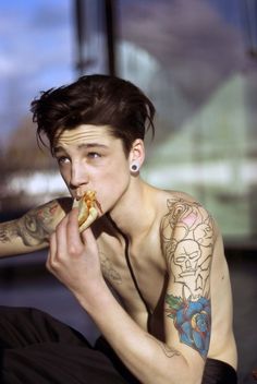 a man with tattoos eating a slice of pizza