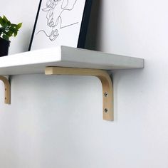 a white shelf with some plants and a drawing on the wall behind it in a corner