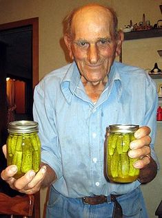 an older man holding two jars filled with pickles