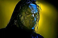 a man with long hair and blue face paint on his face, standing in front of a yellow light