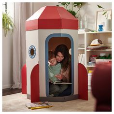 a woman and child are sitting in a play house with a book on the floor