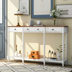 a white console table with two drawers and three vases on it in front of a beige wall