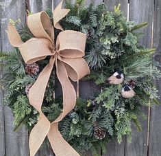 a wreath with pine cones, evergreen leaves and two birds on it hanging from the side of a wooden fence