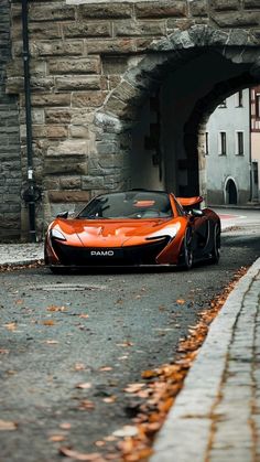 an orange sports car parked in front of a stone tunnel on the street next to a brick building