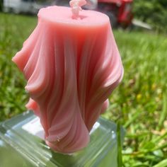 a pink candle sitting on top of a plastic container in the grass next to a red lawn mower