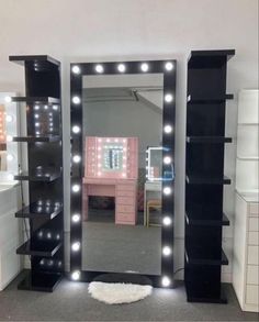 a large mirror with lights on top of it in front of a desk and shelves