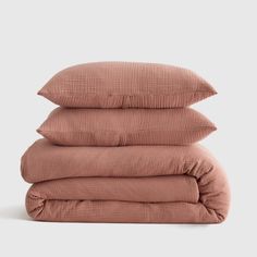 three pillows stacked on top of each other in dusty pink linens, one is folded and the other has a ruffled edge