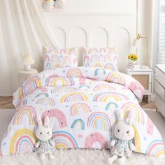 two stuffed animals sitting on top of a bed next to a rainbow comforter set