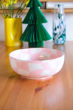 a pink and white bowl sitting on top of a wooden table next to vases