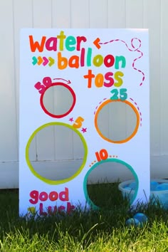 a sign that says water balloon toss on it in front of a white fence and green grass